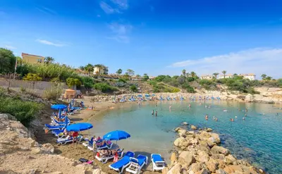 a beach with chairs and umbrellas and people in the water at Hanns Villa in Protaras