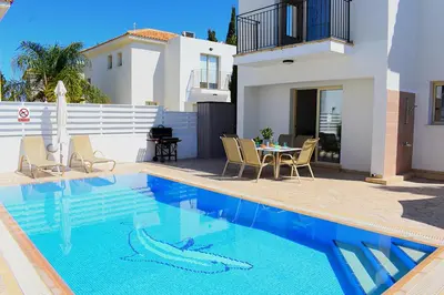 a swimming pool with a table and chairs and a house at Palm Village Escape in Protaras