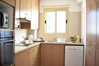 a kitchen with wooden cabinets and a sink and a window at Palm Village Escape in Protaras