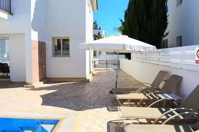 a patio with chairs and an umbrella and a pool at Palm Village Escape in Protaras