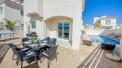 a patio with a table and chairs and a swimming pool at Pernera Holiday Villa 012 in Protaras