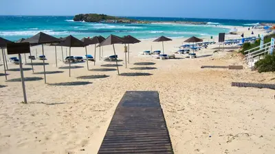 a sandy beach with umbrellas and chairs and the ocean at Ayia Napa Holiday Villa 003 in Ayia Napa