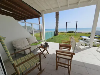 a porch with a couch and chairs and the beach at Ammos Beachfront Villa Paradise in Larnaka