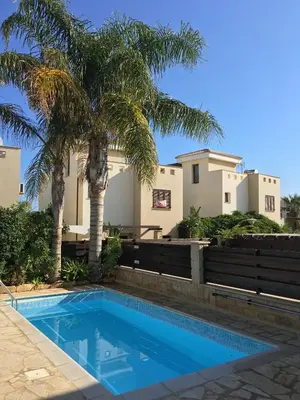 a swimming pool in front of a house with palm trees at Summer Breeze in Paralimni