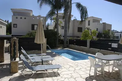 a pool with chairs and a table and an umbrella at Summer Breeze in Paralimni