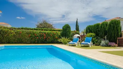 a swimming pool in a yard with two blue chairs at Ayia Napa Holiday Villa 036 in Ayia Napa