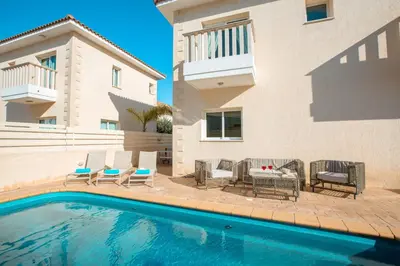 a swimming pool with chairs and a table and a house at Protaras Holiday Villa 035 in Protaras