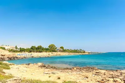 a beach with blue water and trees in the background at Villa Cypriana in Protaras