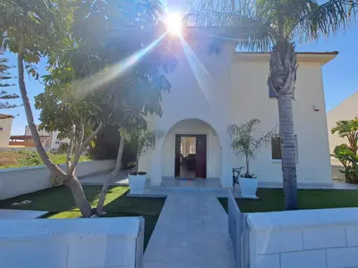 a white house with palm trees in front of it at Sandy Coast Beach Villa in Larnaka