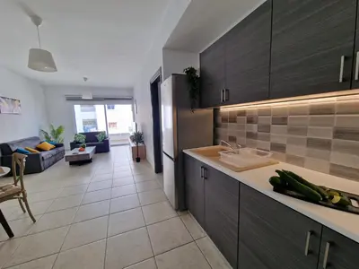 a kitchen with brown cabinets and a living room at Tropical Paradise 200m from Finikoudes beach in Larnaka