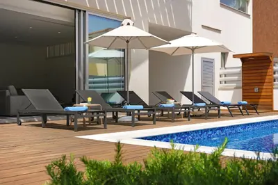 a pool with chairs and umbrellas next to a building at Villa Sunrise Glory - 150m from Trinity Beach in Protaras