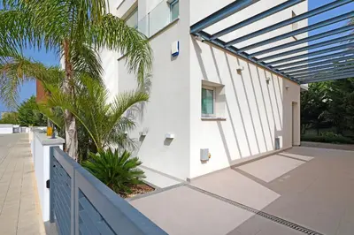 a white building with a blue fence and palm trees at Villa Sunrise Glory - 150m from Trinity Beach in Protaras