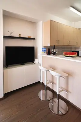 a kitchen with two bar stools and a flat screen tv at Finikoudes Seaview Vibe 1 Bdr Flat in Larnaka
