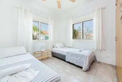 two beds in a white room with two windows at Pernera Blue Villa in Protaras