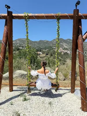 a woman in a white dress sitting on a swing at Safari House with fireplace in Agros