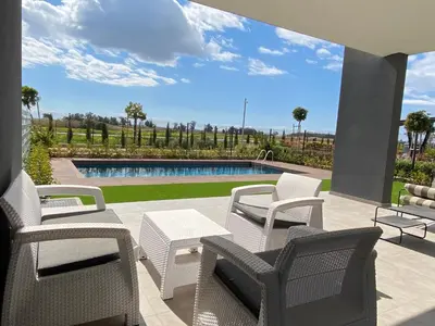 a patio with white chairs and a swimming pool at Sunset Gardens - Holiday Apartments in Limassol