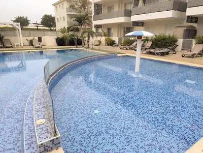 a large swimming pool with an umbrella next to a building at Violetta Apartment, Ground Floor Pool View in Paralimni