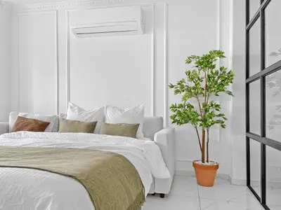 a white bedroom with a bed and a potted plant at The Encino - luxury seaside suite in Larnaka