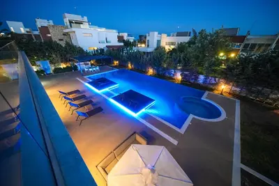 a swimming pool at night with chairs and an umbrella at Royal Oasis Villa in Ayia Napa