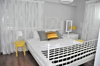 a white bedroom with a white bed with yellow pillows at Liliana Sea View Suite in Larnaka