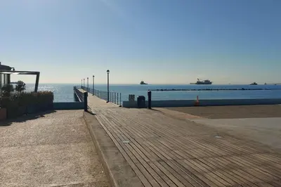 a wooden boardwalk next to the ocean with ships at Tourist Hot Spot Location in Limassol