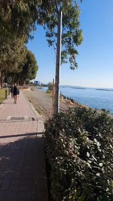 a person walking down a sidewalk next to the water at Balcony Sea View Whole Apt, Minutes To Beach in Limassol