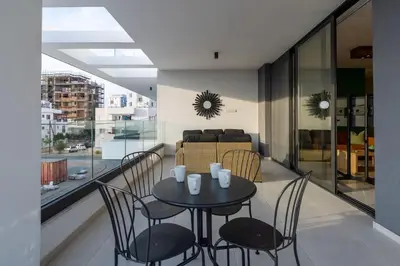 a table and chairs on a balcony with a couch at Beachcomber 2-Bedroom Apartment in Larnaca in Larnaka