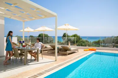 a man and woman sitting at a table next to a pool at Exquisite Protaras Villa Villa Bulat 4 Bedrooms Beachfront in Protaras