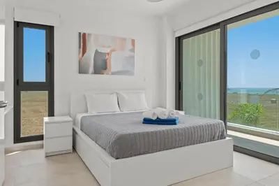 a white bedroom with a bed and a large window at Serenity Waves Villa 9 in Sophtadhes