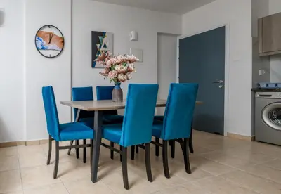 a dining room table with blue chairs and a vase of flowers at Olympia Flat 104 in Larnaka