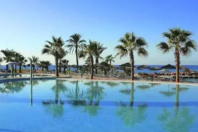 a large swimming pool next to a beach with palm trees at SPECIAL OFFER -70 Percent Off - 2 BR - Sleep 7 - Best Location at Ayia Napa City Center in Ayia Napa