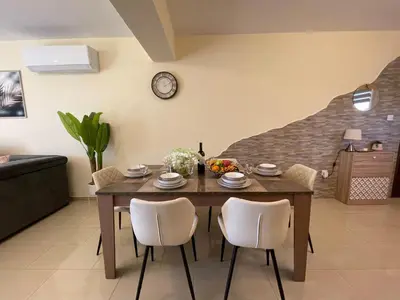 a dining room table with chairs and a clock on the wall at Nissi Beach beautiful apartment in Ayia Napa