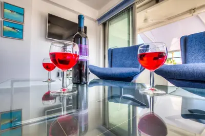 a bottle of wine and three wine glasses on a glass table at Beachfront Trident in Protaras