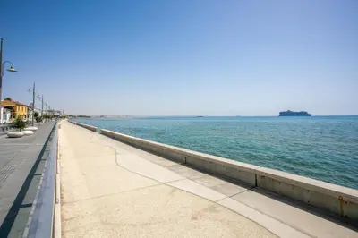 a sidewalk next to the water with a ship in the distance at Palmove Newly Build Seaview Apt in Larnaka