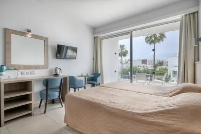 a bedroom with a bed and a desk and a balcony at Bellini Hotel in Ayia Napa