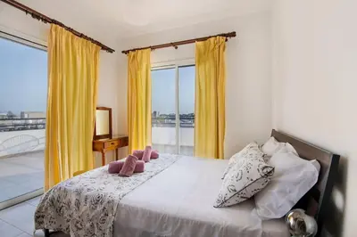 a bedroom with a bed with yellow curtains and a balcony at City Center Top Floor Big Balcony 2BR Close to the Beach in Larnaka