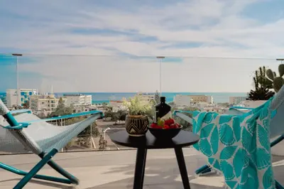 a balcony with two chairs and a table with a bowl of fruit at Protaras Eden Seaside Suite in Protaras