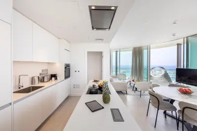 a kitchen and living room with white cabinets and a table at Ayia Napa Marina East Tower Suite in Ayia Napa