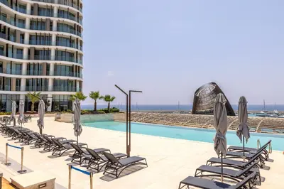 a pool with chairs and umbrellas next to a building at Ayia Napa Marina East Tower Suite in Ayia Napa
