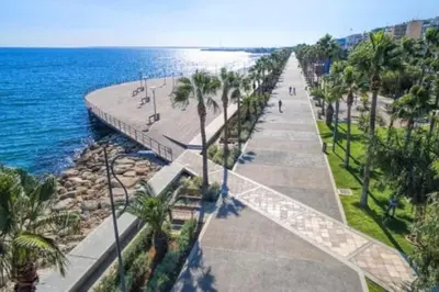 a walkway next to the ocean with palm trees at Luxury one bedroom - seafront in Limassol