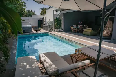 a swimming pool with chairs and an umbrella at TG NEW Luxury Private Resort & SPA Villas - Heated Salty Swimming Pool, Outdoor Jacuzzi, Sauna, Exotic Garden in Limassol