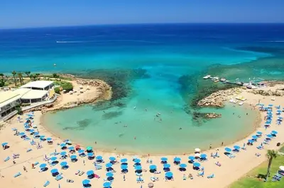 a beach with umbrellas and people in the water at Crystal aptmnt next to the beach in Protaras