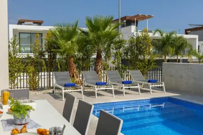 a patio with chairs and a swimming pool with palm trees at Protaras Bay View Villa 11 in Protaras