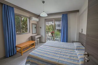 a bedroom with a bed and a desk and windows at Merab Napa Suites in Ayia Napa