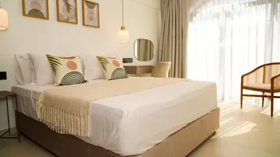 a white bedroom with a large bed and a chair at Sirena Bay Beach House and Luxury Suites in Protaras