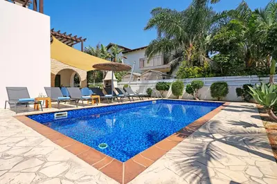 a swimming pool in a yard with chairs and an umbrella at Villa Evia - Walking to Med Sea in Ayia Napa