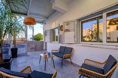 a patio with chairs and a table and windows at FatCow Beach Apartment in Larnaka