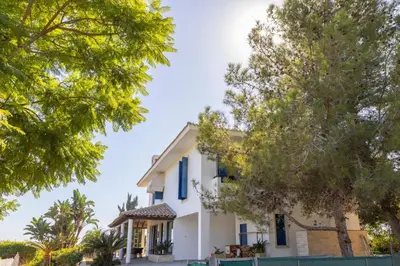 a white house with blue shutters and trees at Ayia Napa Sycamore SeaView in Ayia Napa