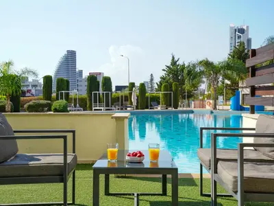 a hotel pool with two chairs and a table with drinks at Aqua House Valentino in Limassol