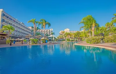 a large swimming pool with palm trees and buildings at Tsokkos Gardens Hotel in Protaras